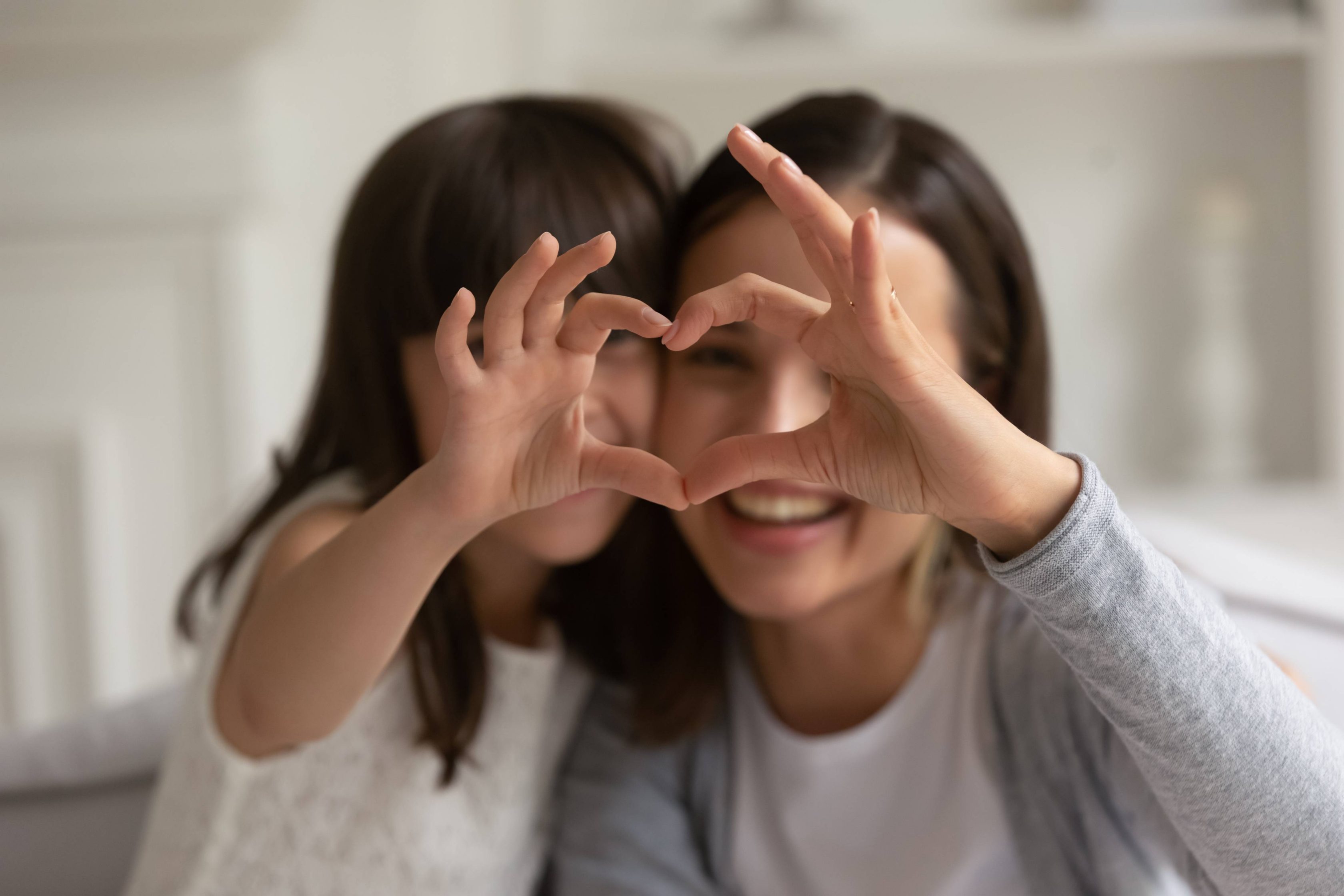 Ευτυχισμένη νεαρή μητέρα με τη χαριτωμένη μικρή κόρη της, σχηματίζουν καρδιά με τα χέρια τους, κοιτάζοντας την κάμερα.