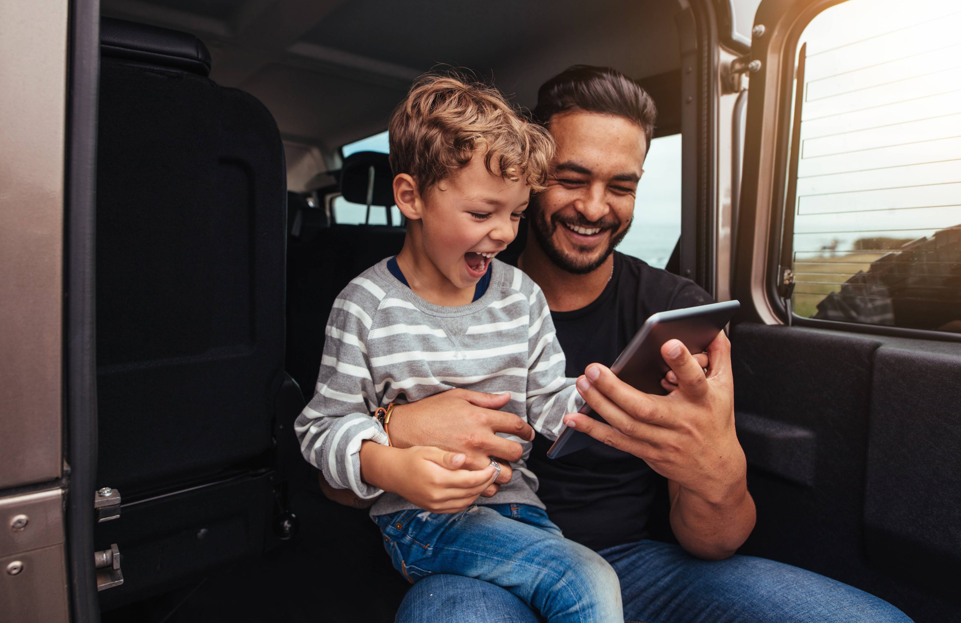Ένας πατέρας κάθεται χαρούμενος με τον μικρό γιο του στο πορτ-μπαγκάζ, κοιτάζοντας μία ψηφιακή ταμπλέτα.