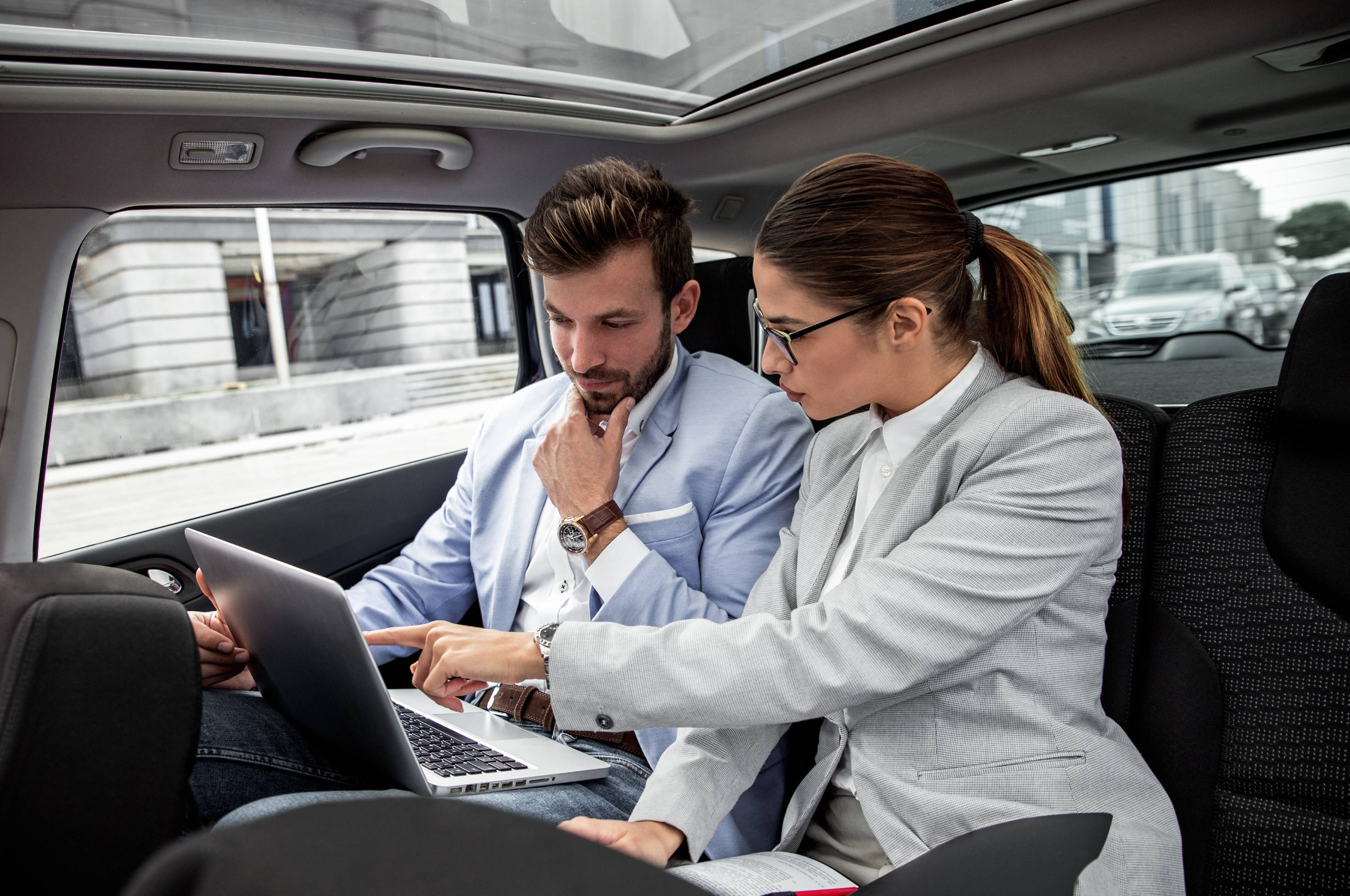 Young business people working together while traveling by a car. They are using laptop and preparing for meeting.
