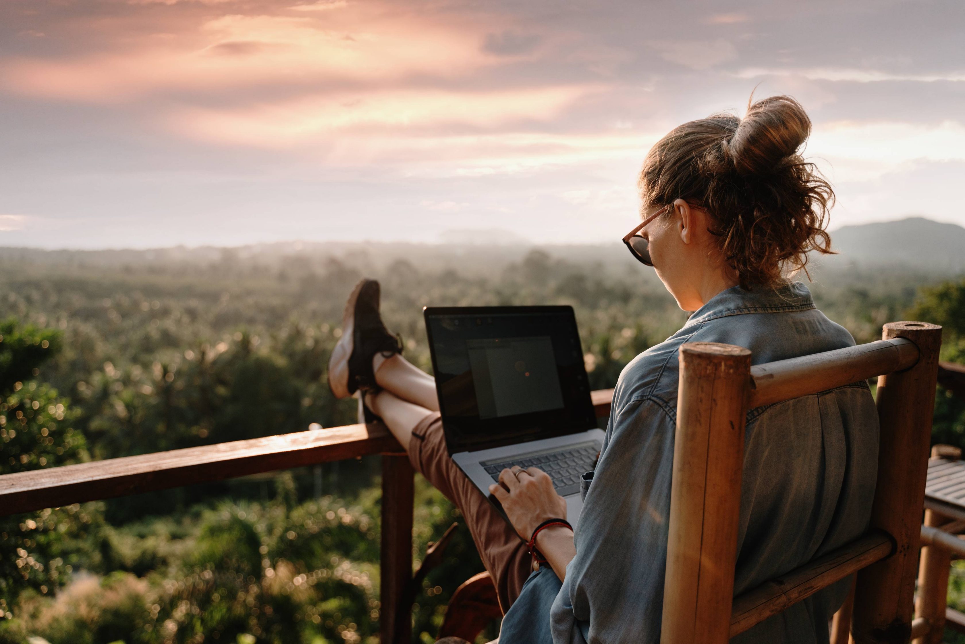 Young business woman working at a laptop at sunrise on the top of the mountain with a sea view.